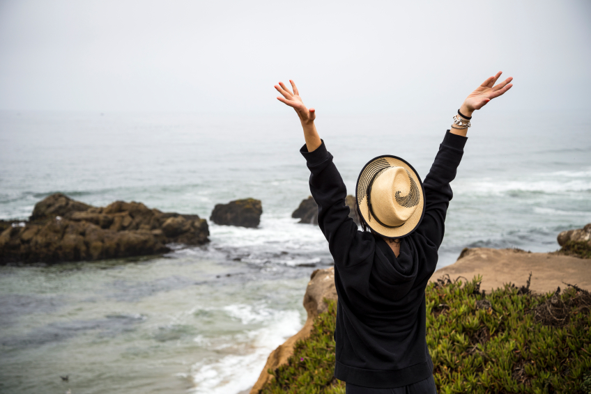 Imagen de chica de espaldas levantando los brazos frente al mar